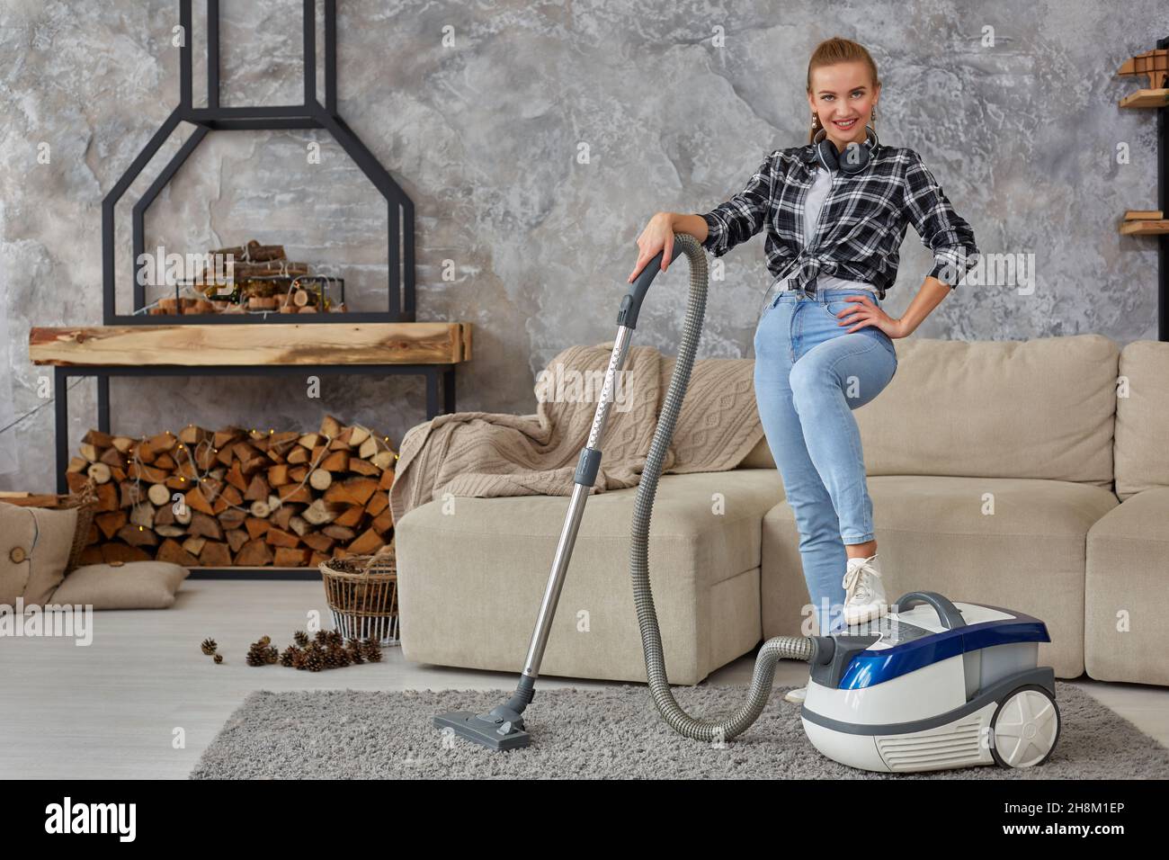 Young smiling woman vacuum cleaning the carpet in the living room ...