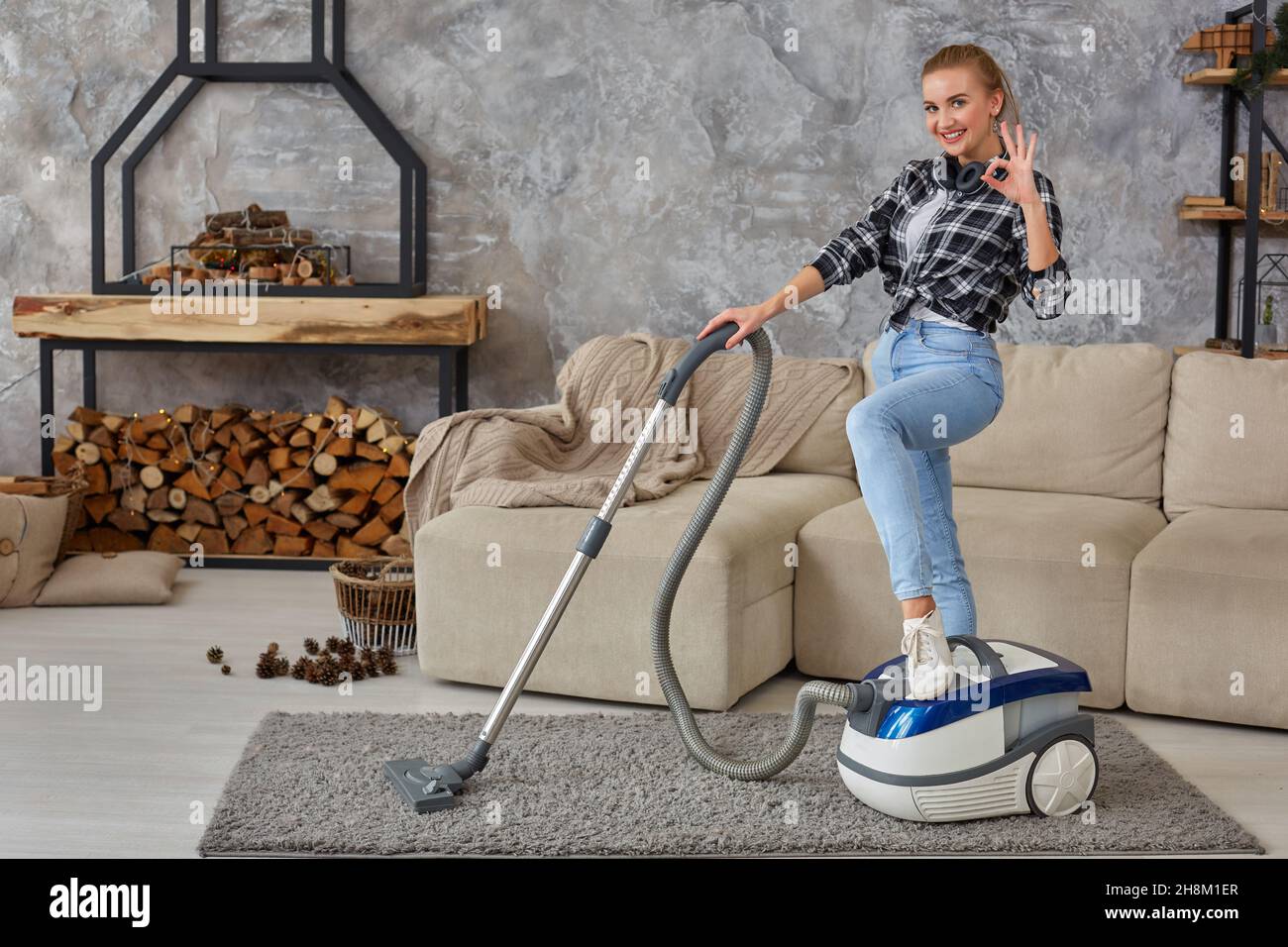 Young smiling woman vacuum cleaning the carpet in the living room ...