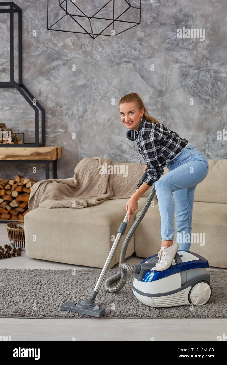 Young smiling woman vacuum cleaning the carpet in the living room ...