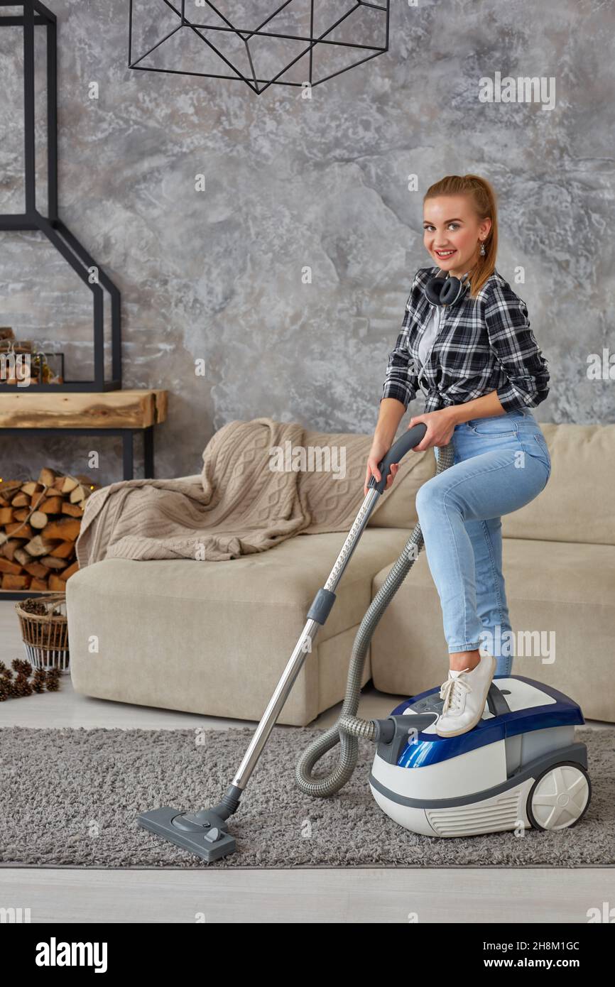 Young smiling woman vacuum cleaning the carpet in the living room ...