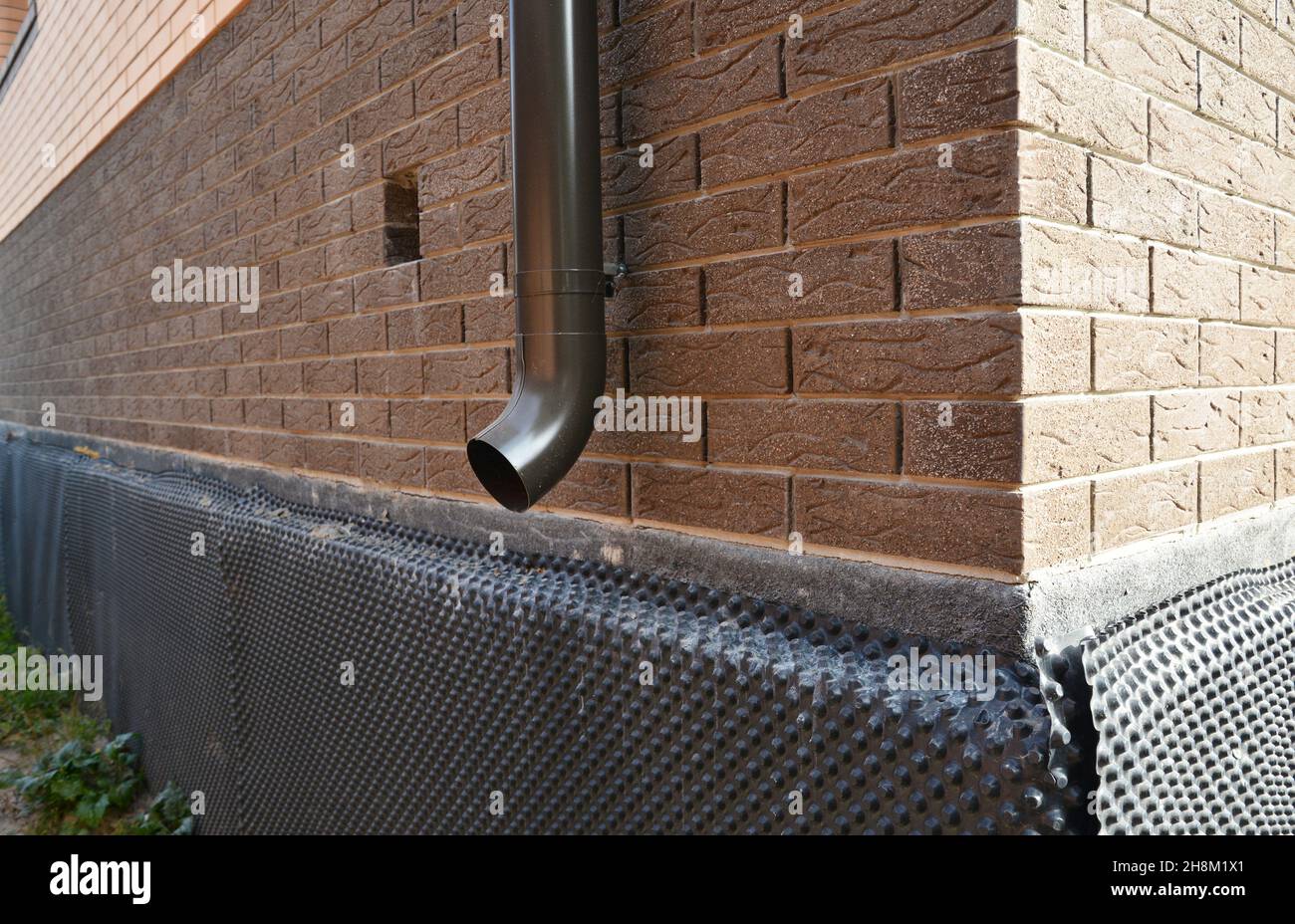 A closeup of a metal downspout, roof gutters downspout installed near unfinished foundation