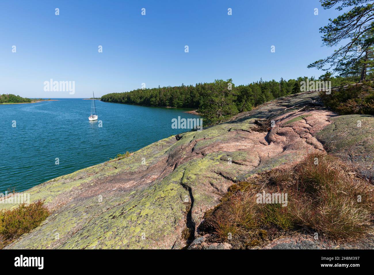 View of a moored sailboat at sea and forested shoreline from a cliff along the Grottstigen cave nature trail at Geta in Åland Islands, Finland. Stock Photo