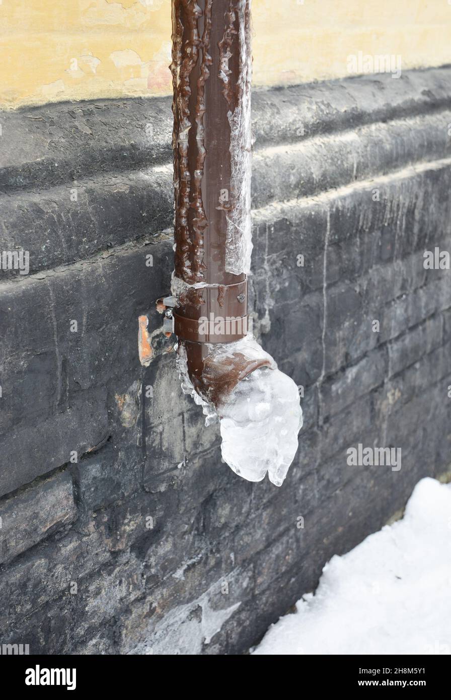 A closeup of a plastic roof gutter downpipe, downspout with frozen
