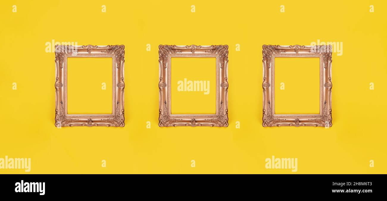 three empty ornate gold picture frames on yellow wall background Stock Photo