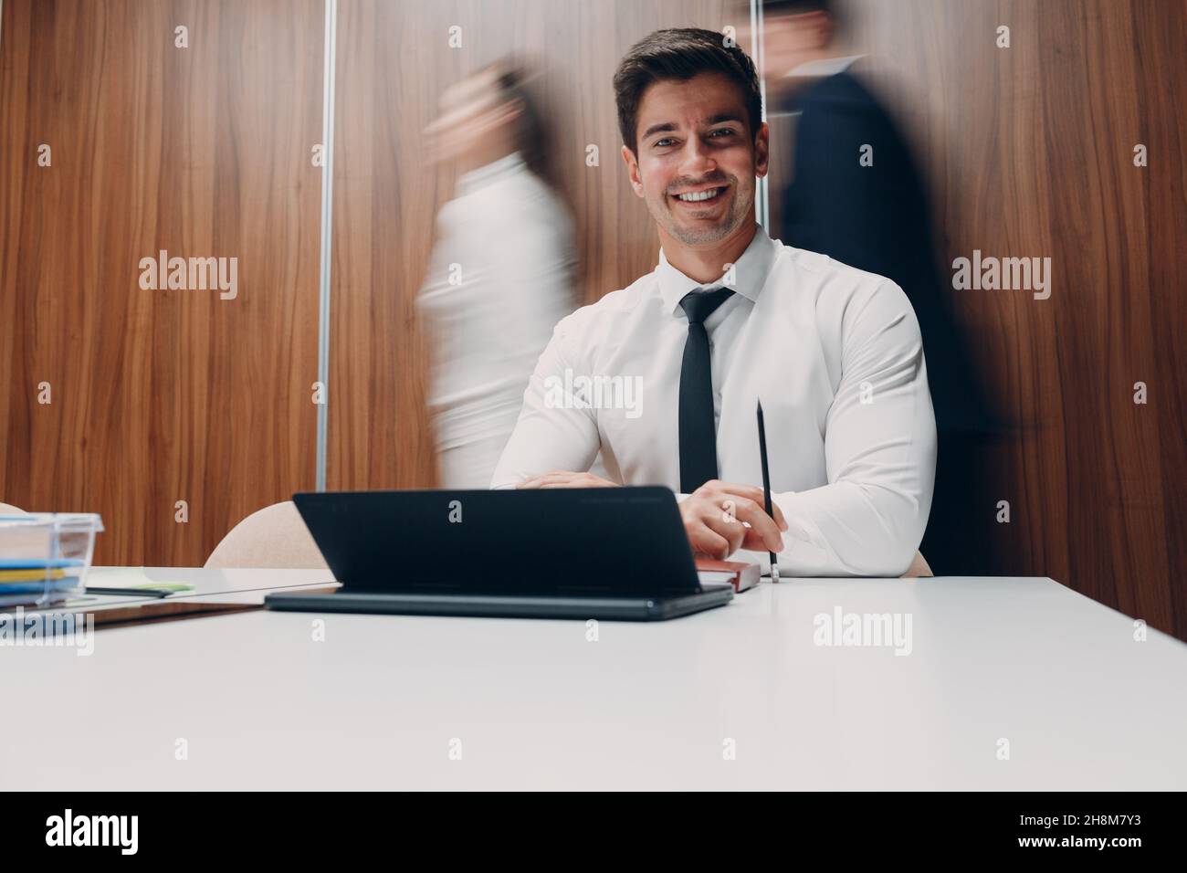 Businessman using laptop sit at table in office meeting background with walking people with motion blur. Business people man and woman group conference discussion. Stock Photo