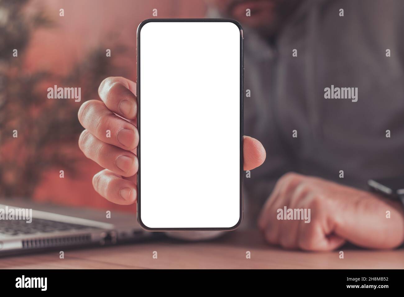 Mock up blank screen of modern smart phone in male hands over laptop computer, freelancer using mobile phone, top view Stock Photo