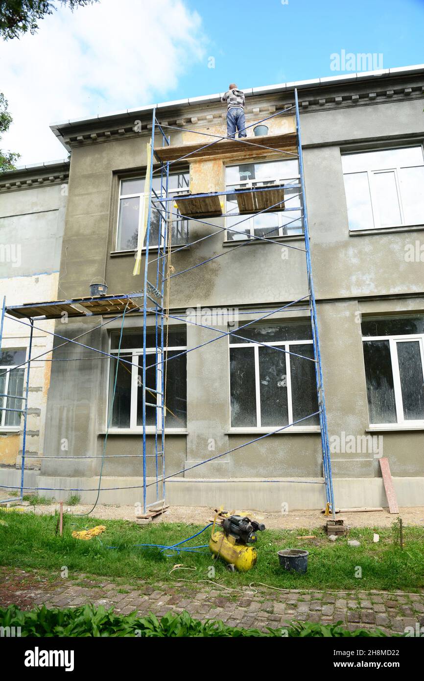 Facade rendering and renovation. A building contractor on scaffolds is finishing in stucco, plaster the exterior wall of the house before painting. Stock Photo