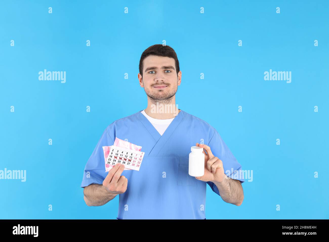 Doctor holds menstrual calendar, pads and bottle of pills on blue background Stock Photo