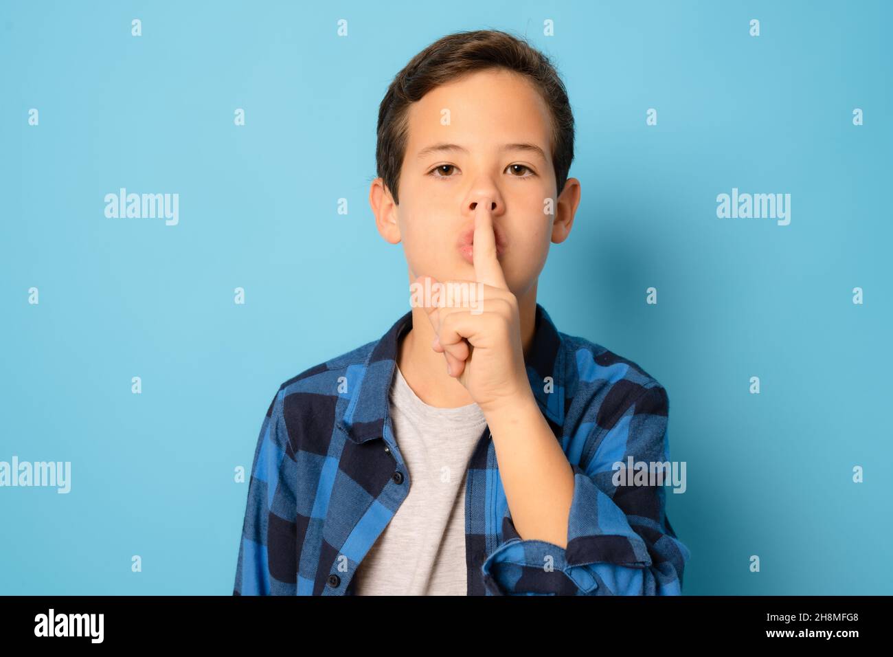 Kid boy asking to be quiet with finger on lips, isolated on blue