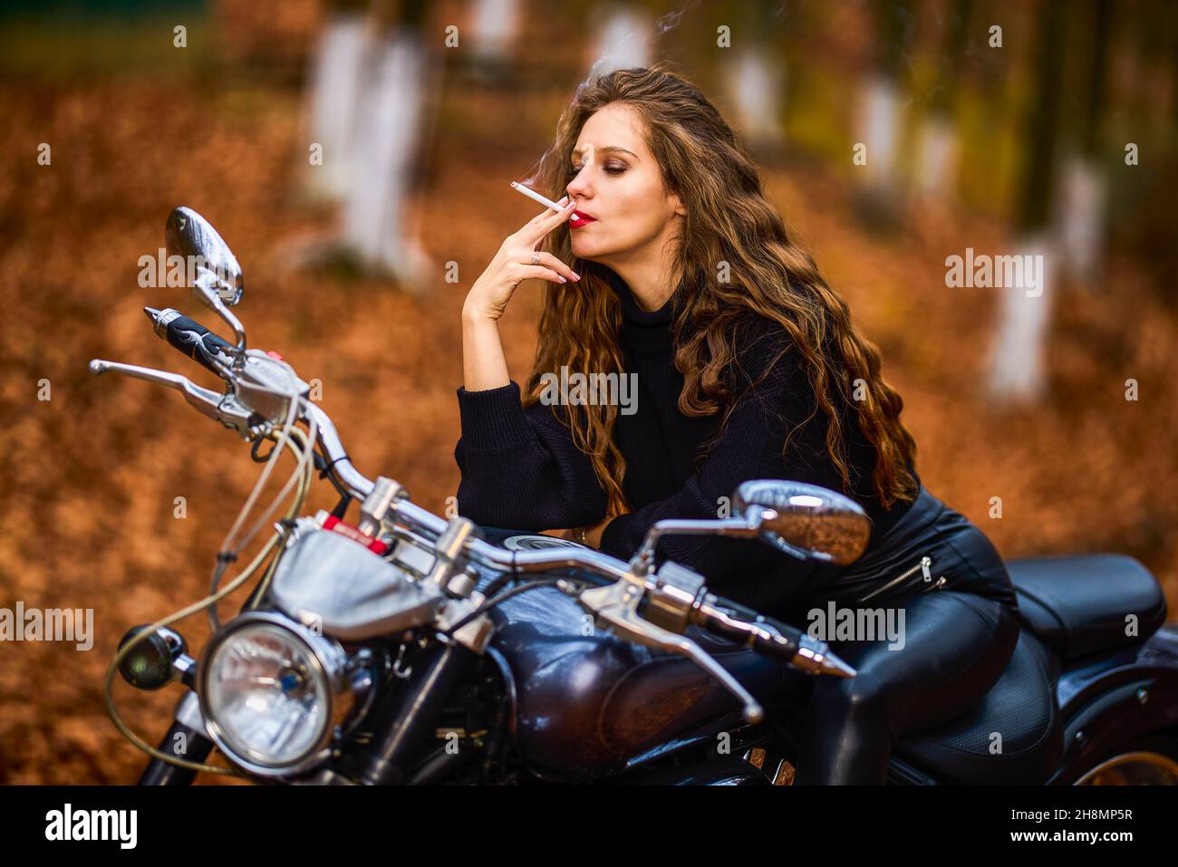 A Beautiful Long Haired Woman Smoking On A Chopper Motorcycle In Autumn Landscape On A Forest