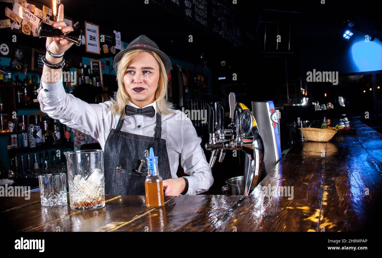 Charming woman barkeeper is pouring a drink behind the bar Stock Photo