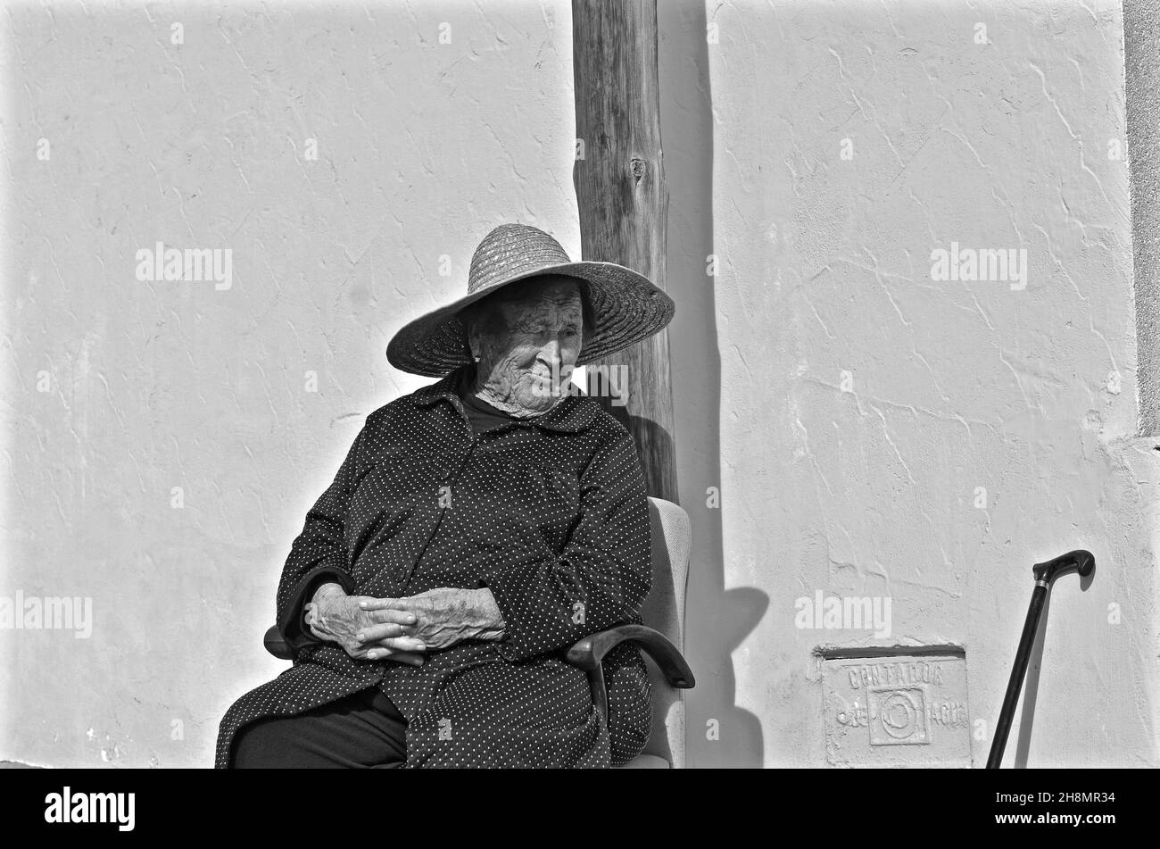 Old woman with folded hands sitting on chair with sun hat, El Largo, Andalusia, Spain Stock Photo