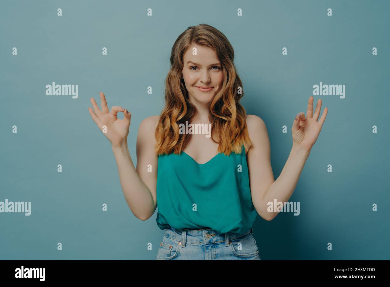 Confident joyful young woman in casual clothes gesturing ok sign with both hands in studio Stock Photo