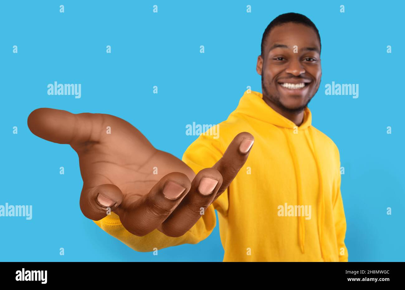 Happy black guy showing big outstretched hand, offering help, taking or giving something, reaching out for support Stock Photo