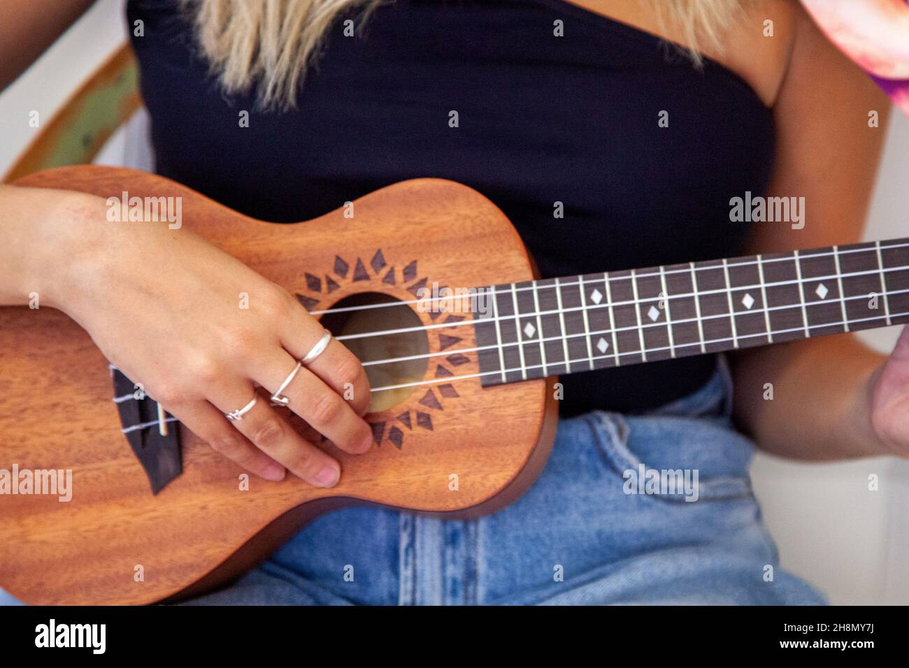 Woman playing the ukulele sitting on the bed in her room at home Stock