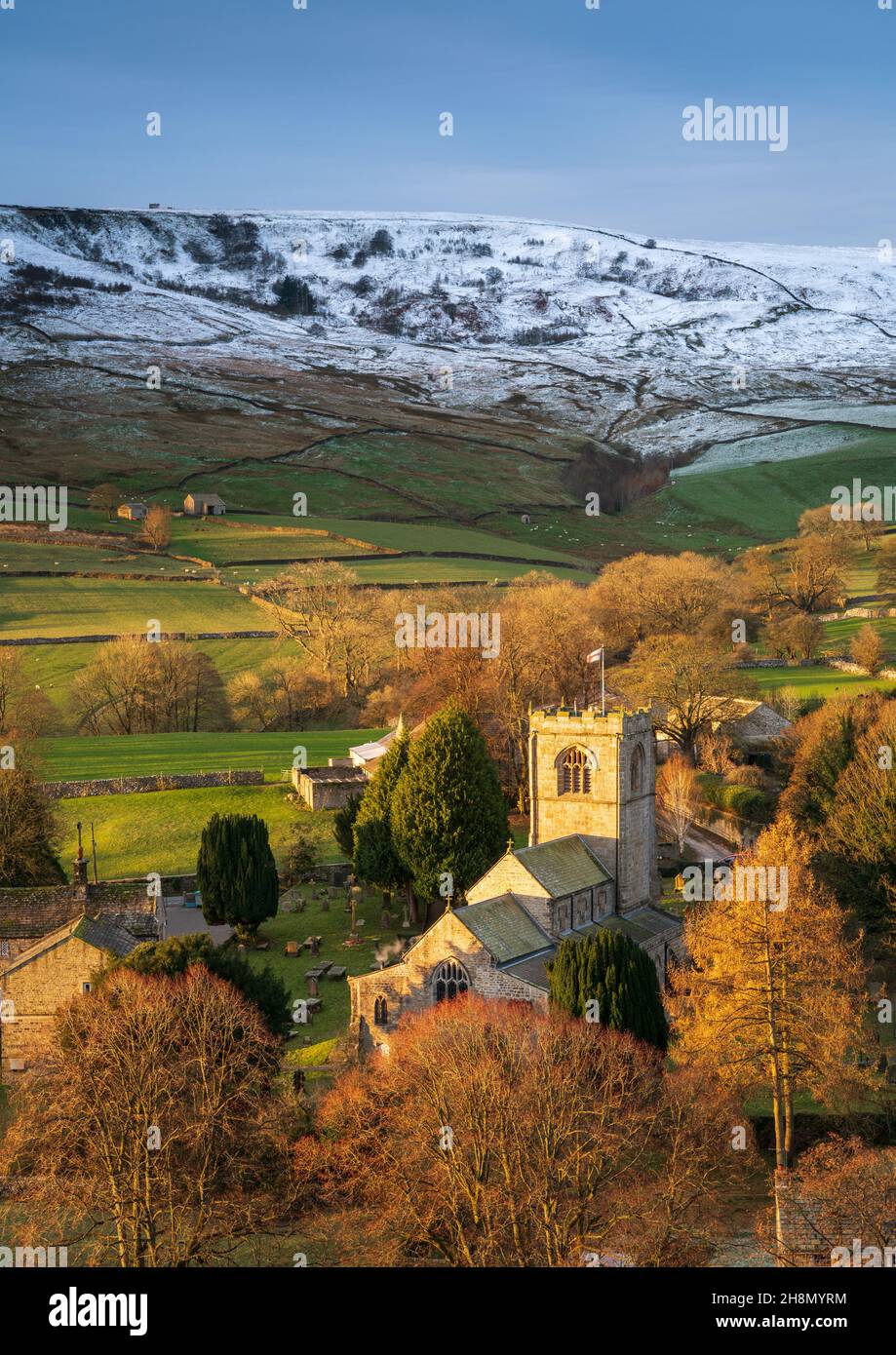 A brief burst of light at sunrise illuminates St. Wilfrid's Church in the pretty village of Burnsall with the hills behind covered in early snowfall. Stock Photo