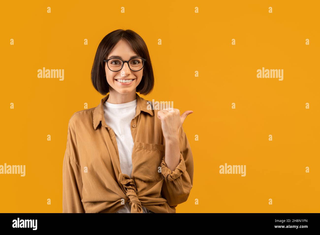 Check this offer. Positive young woman pointing thumb finger aside at free space, advertising your text or design Stock Photo