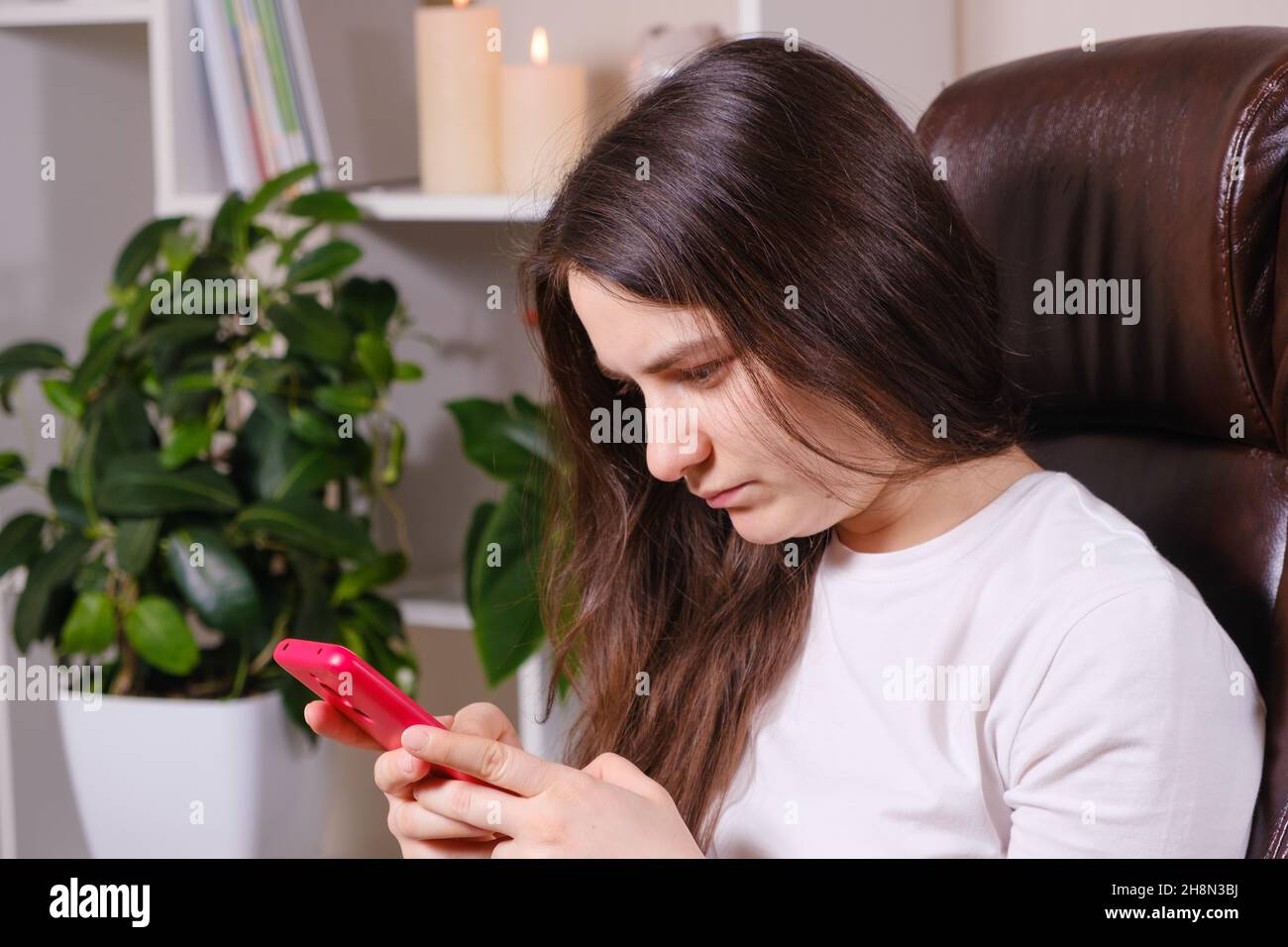 The woman looks at the screen of the phone, tilting her head down, tension of the muscles of the neck and poor posture. Stock Photo