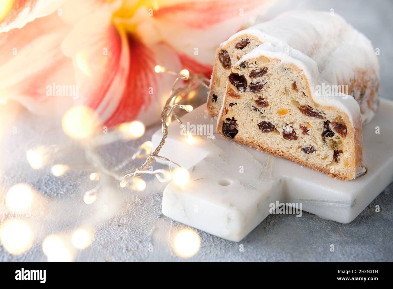 Christmas stollen on off white stone background with amaryllis flower and Xmas garland. Stock Photo