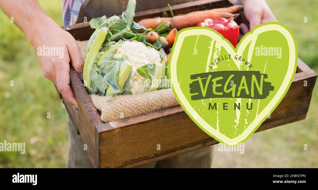 Midsection of man holding crate full of fresh vegetables with vegan menu in heart shape symbol Stock Photo