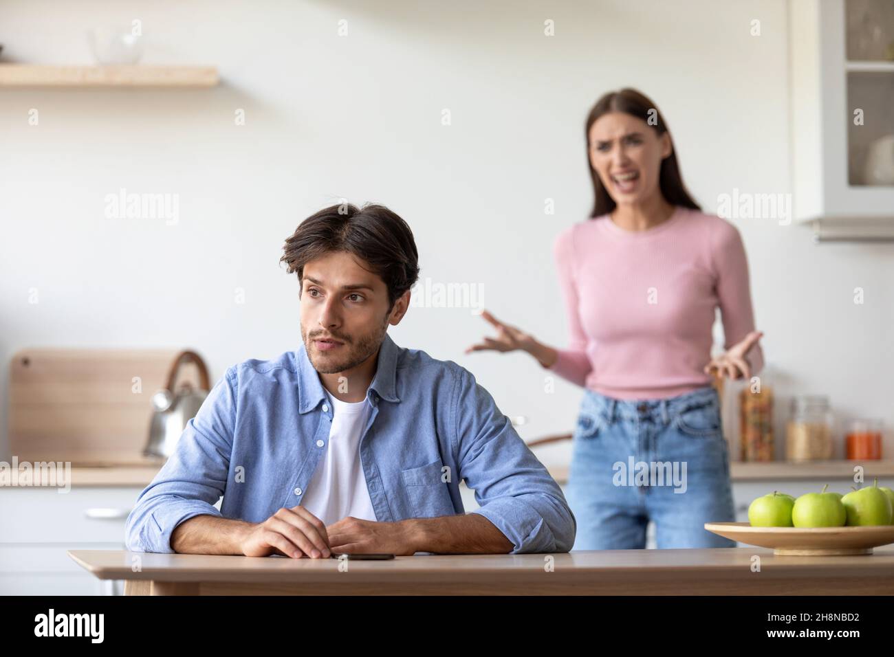 Angry aggressive millennial european wife yells at sad depressed husband at kitchen Stock Photo