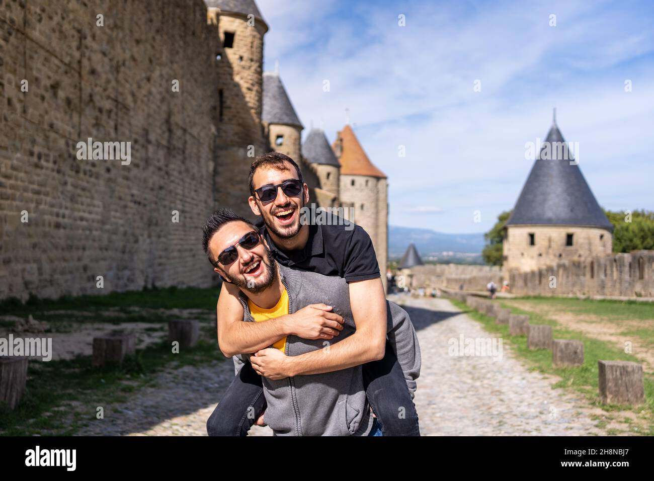 Male jumping on the back of his male couple next to a medieval wall with towers. France Stock Photo
