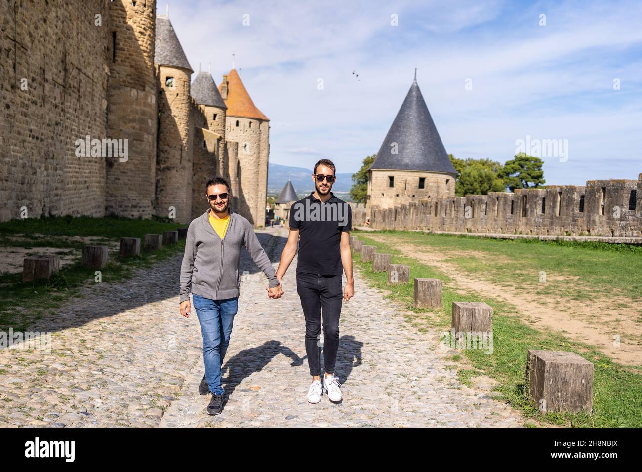 Gay couple walking holding hands next to the walls of a medieval castle. France Stock Photo