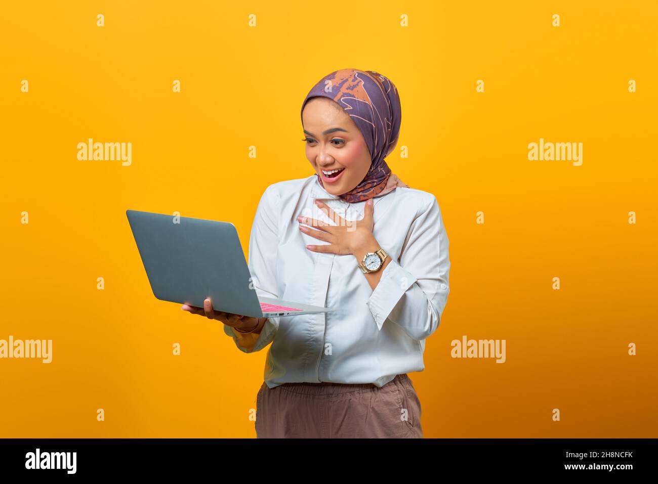 Portrait of excited Asian woman holding laptop over yellow background ...
