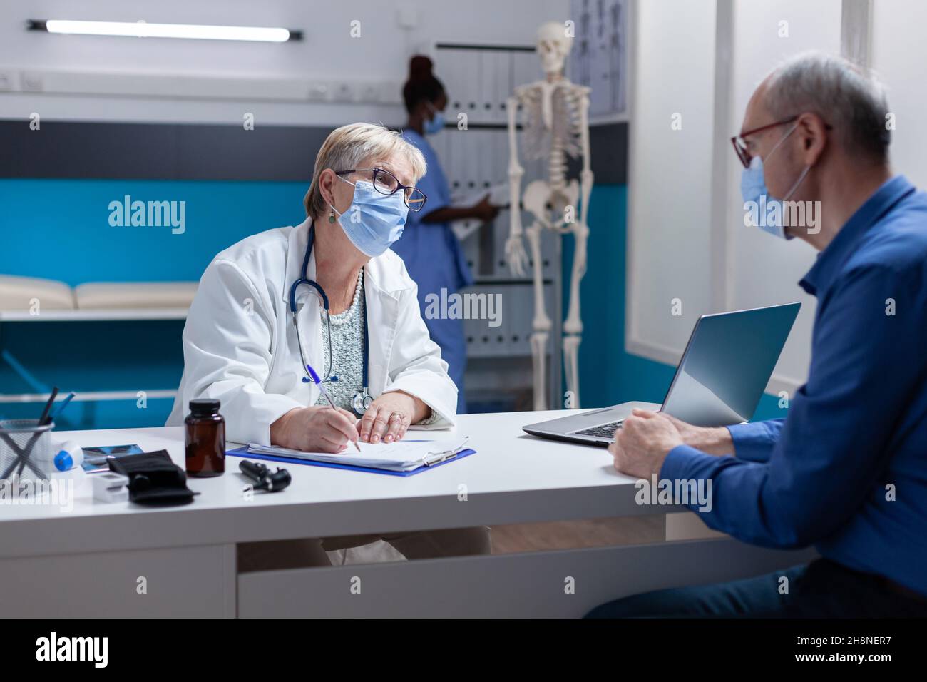 Woman doctor with face mask taking notes on papers at medical ...