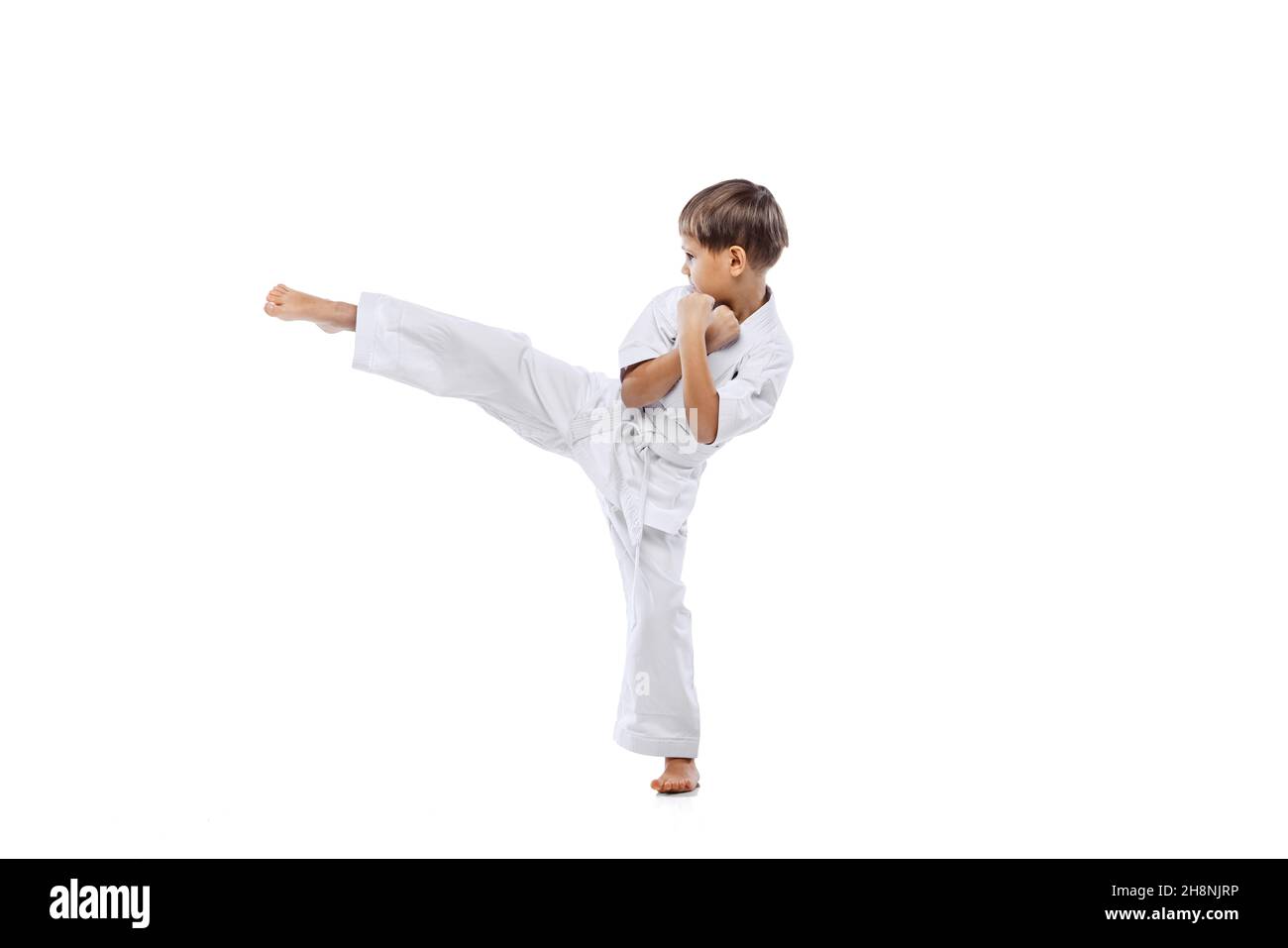 Full-length portrait of little boy, sportsman training, practising martial art, karate isolated over white background Stock Photo