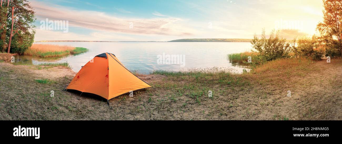 Orange tourist tent on sandy shore of lake at sunrise Stock Photo