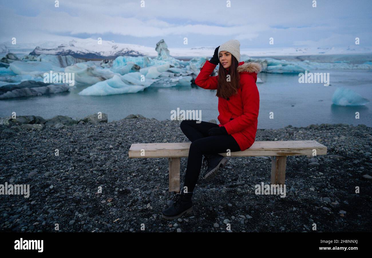 Smile girl sitting on bench in Jokulsarlon glacier lagoon in Iceland. Sustainable travel concept. Tourist offset carbon footprintto Stock Photo