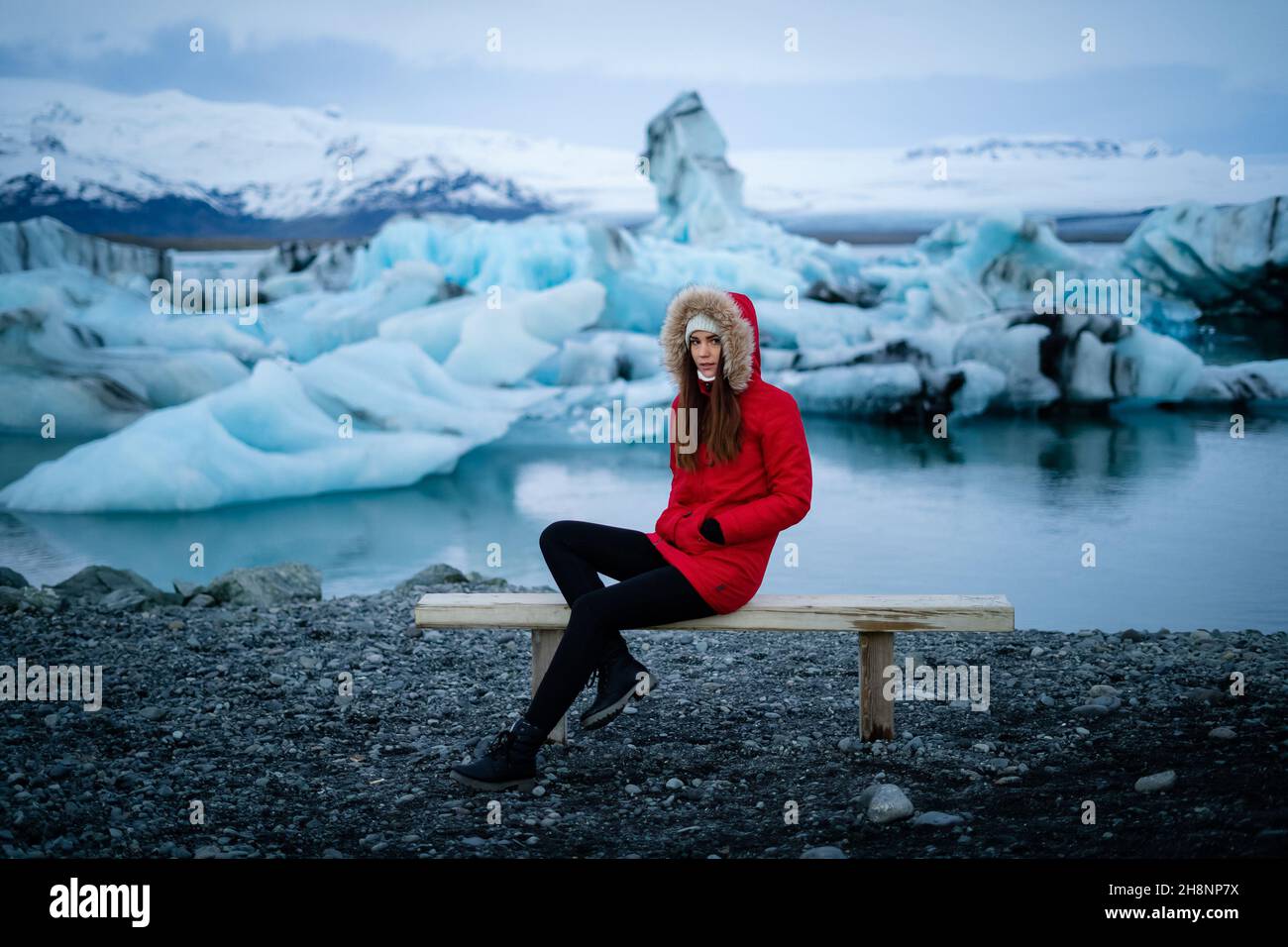 Smile girl sitting on bench in Jokulsarlon glacier lagoon in Iceland. Sustainable travel concept. Tourist offset carbon footprintto Stock Photo