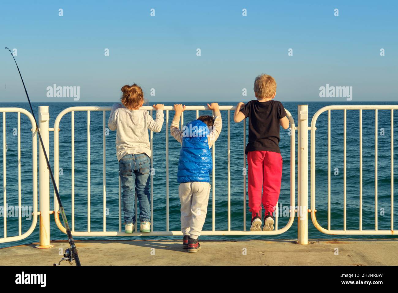 Three small children on the pier have cast their fishing rod and gaze at  the surface of the sea Stock Photo - Alamy