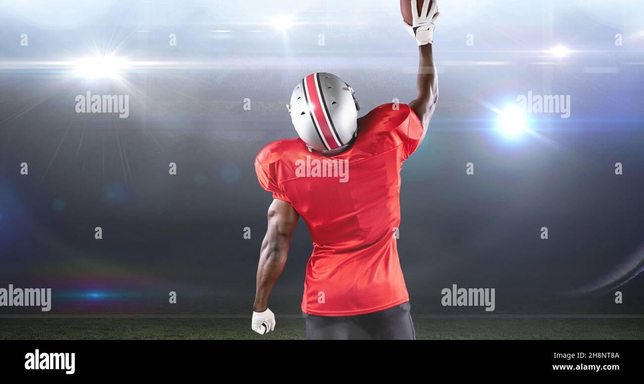 Rear view of male american football player celebrating goal by lifting ball at illuminated stadium Stock Photo