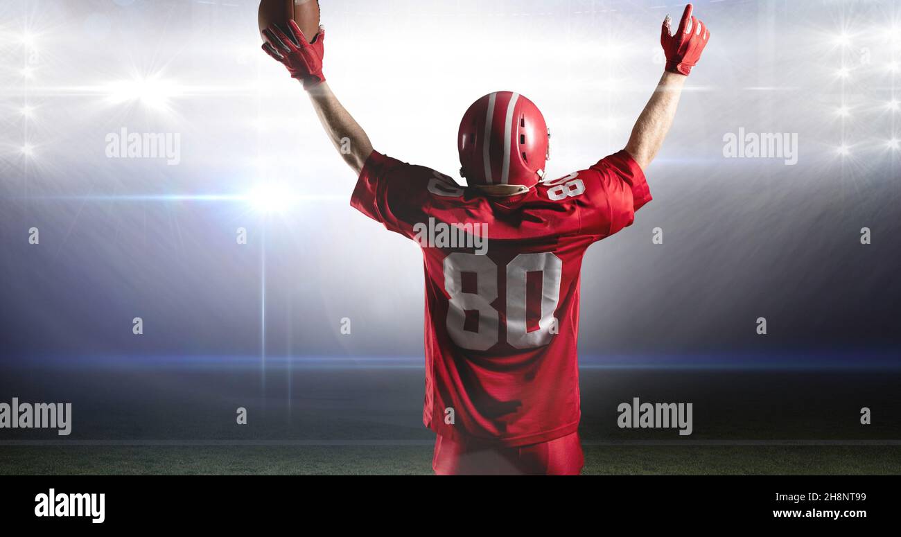 Rear view of male american football athlete celebrating goal by lifting ball at illuminated stadium Stock Photo