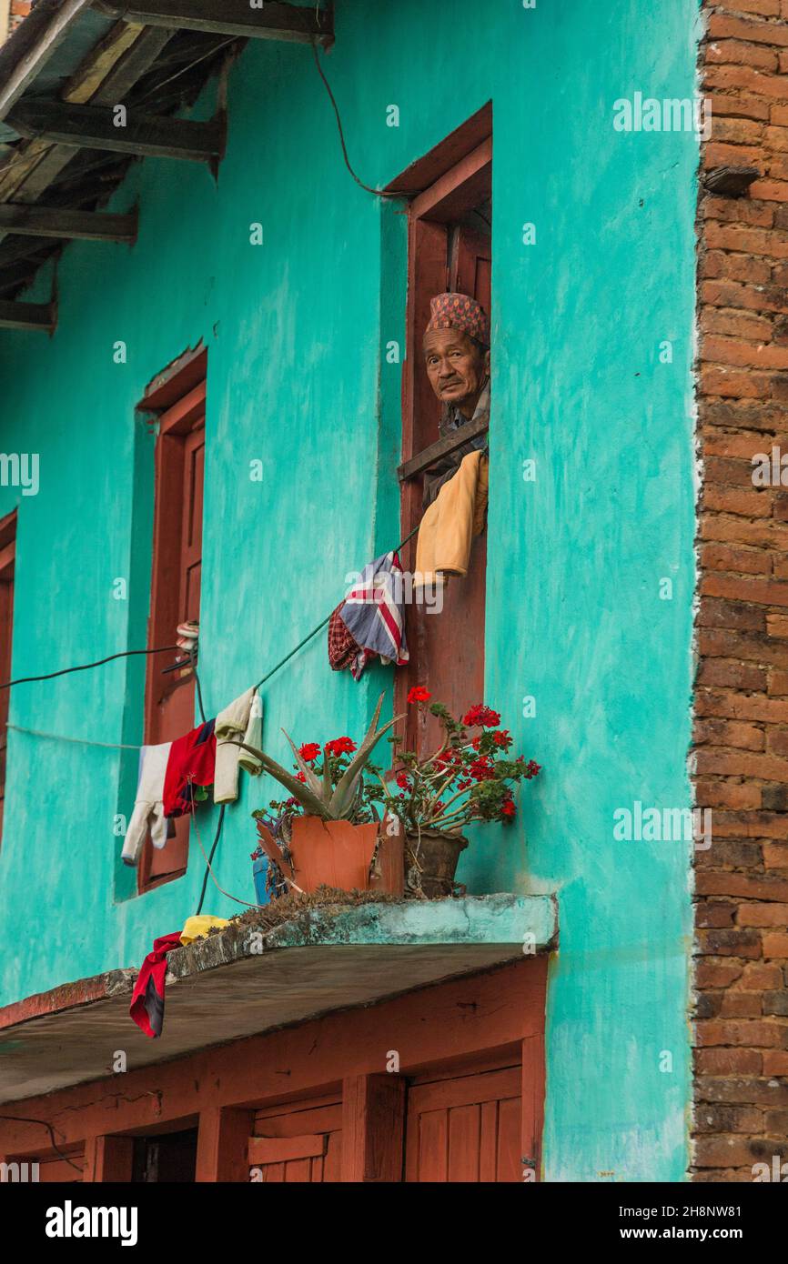 A Newari man wearing a Dhaka topi hat looks out the window of his house in Bandipur, Nepal. Stock Photo