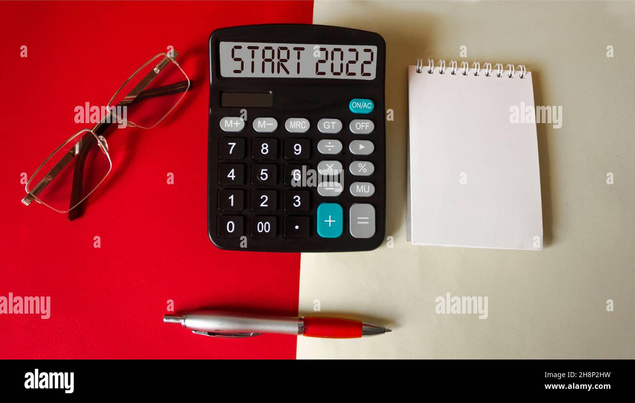 The text START 2022 on the calculator screen on a red and white background  with a notepad, glasses and a pen Stock Photo - Alamy
