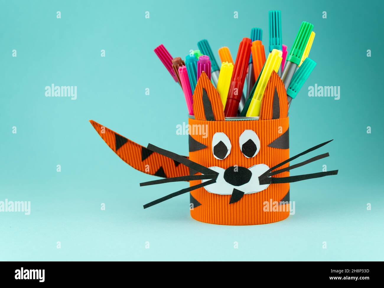 Step-by-step instructions on how to make a stand for stationery from a tin can. Tiger made of paper and cardboard, scissors and glue. A fun DIY craft for children. Do it yourself paper tiger. Stock Photo