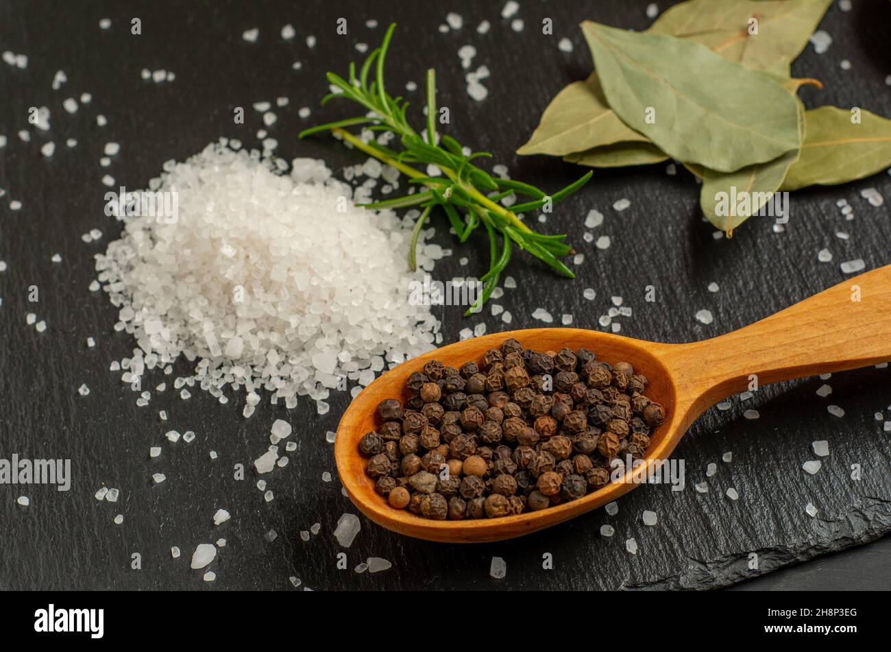 Fresh rosemary, bay leaf salt and pepper in spoon on slate background close up. Shallow focus. Stock Photo