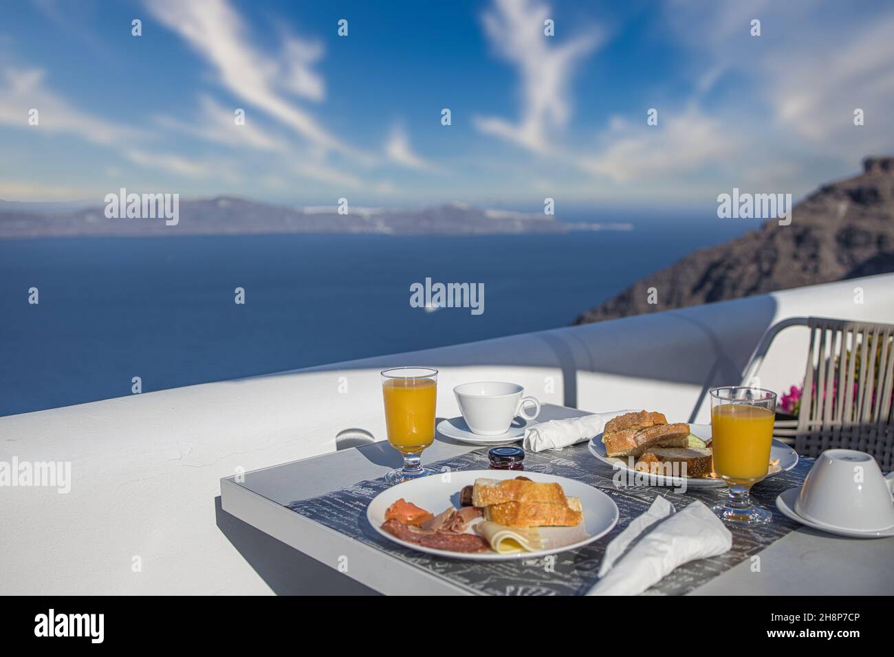 Breakfast table romantic view under idyllic blue sky sea. Perfect luxury breakfast food table for two outdoors. Amazing caldera view on Santorini Oia Stock Photo