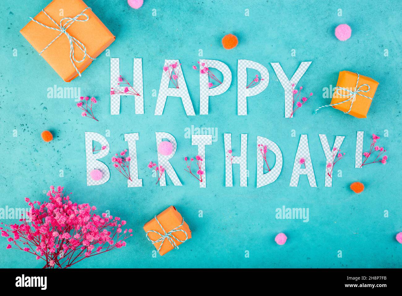 Happy birthday background with letters, orange gifts, pink flowers on turquoise blue background Stock Photo