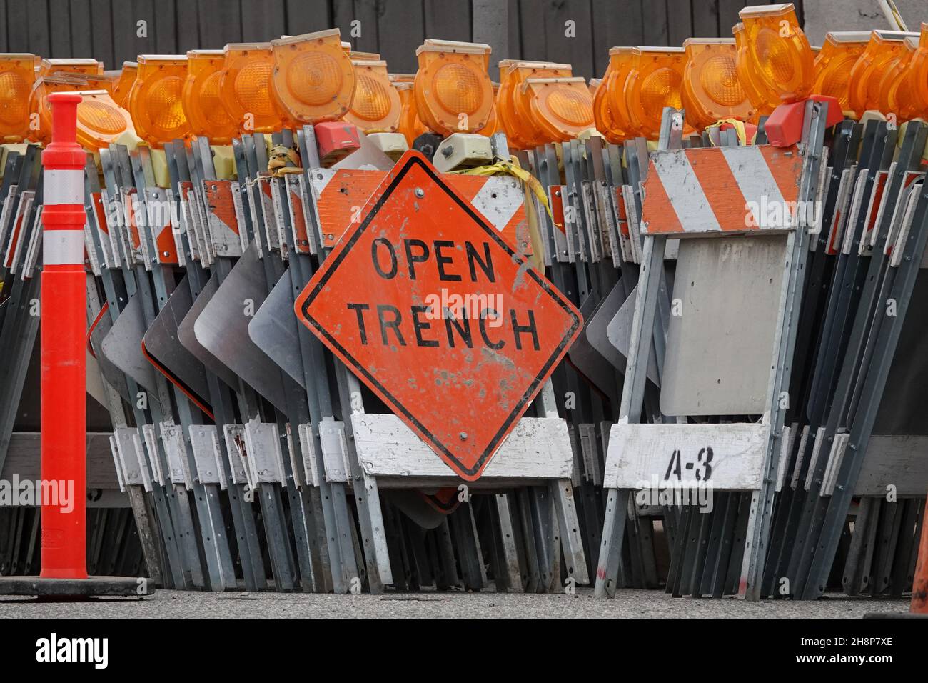 Orange and yellow traffic control barricades, topped with flashing lights, are shown with an OPEN TRENCH sign and a delineator pylon cone. Stock Photo