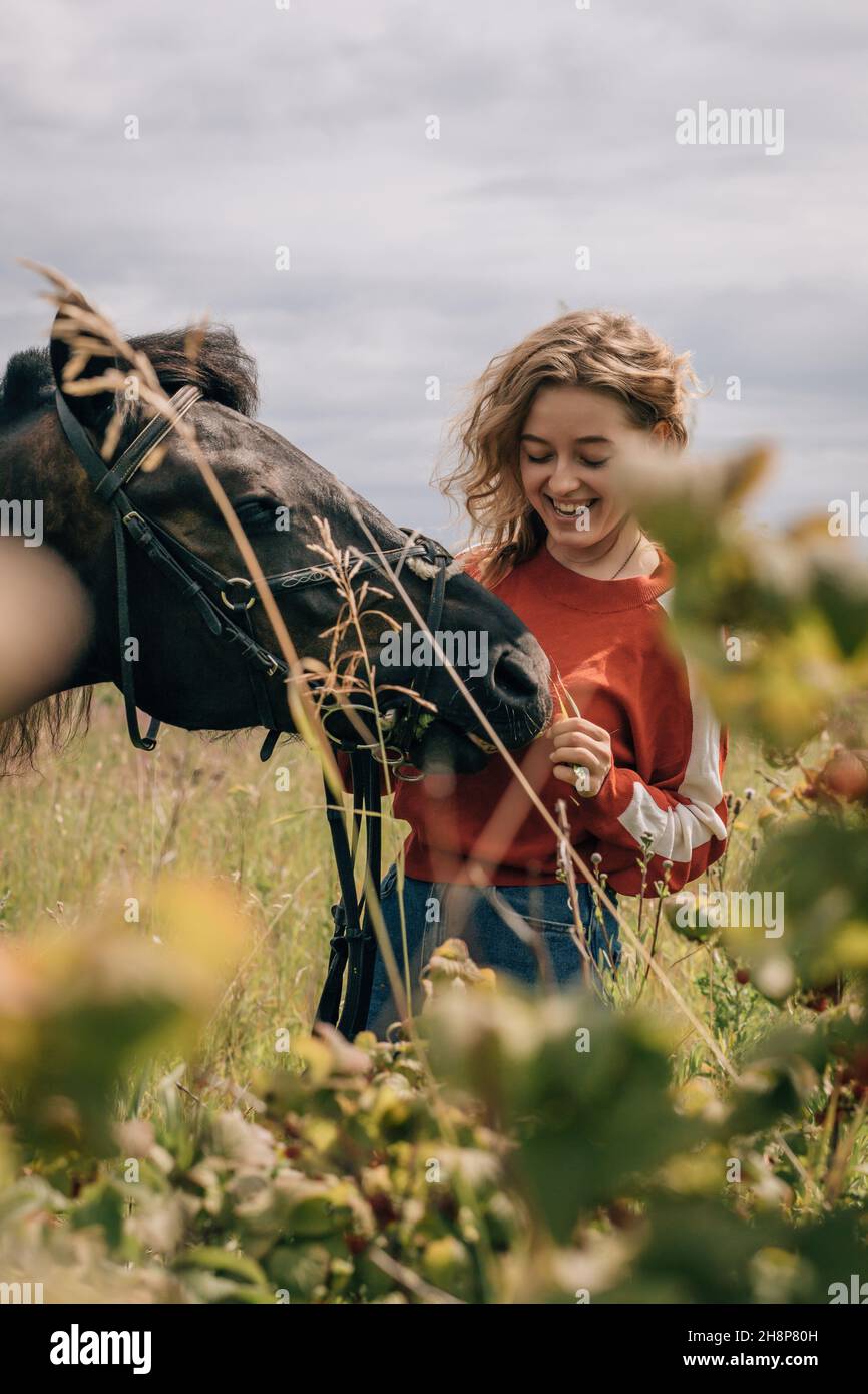 Woman laughing at horse in field, lifestyle, vertical shot. Stock Photo
