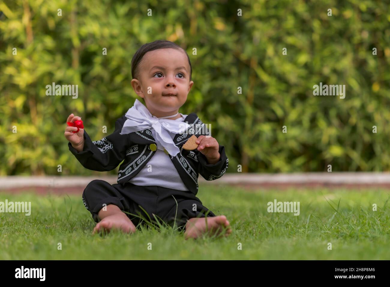 Small latin baby boy with a mariachi costume playing on the grass Stock Photo