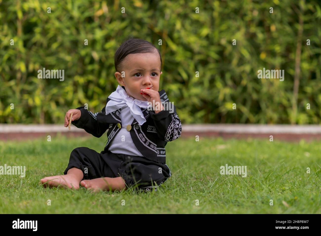 Latin baby boy with a mariachi costume playing with a red flower Stock Photo