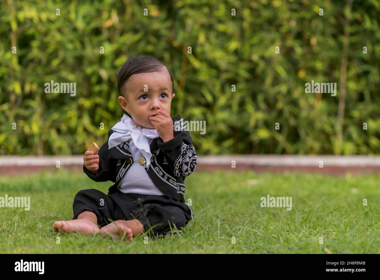 Cute Latin baby boy with a mariachi costume eating a cookie Stock Photo