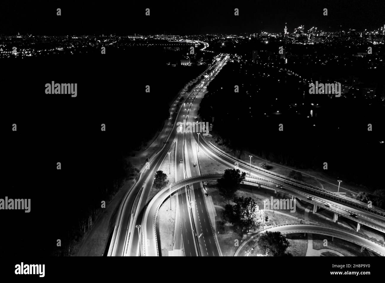 Aerial drone night shot of multilevel illuminated ring highway road junction leading to the sea. Black and White Stock Photo