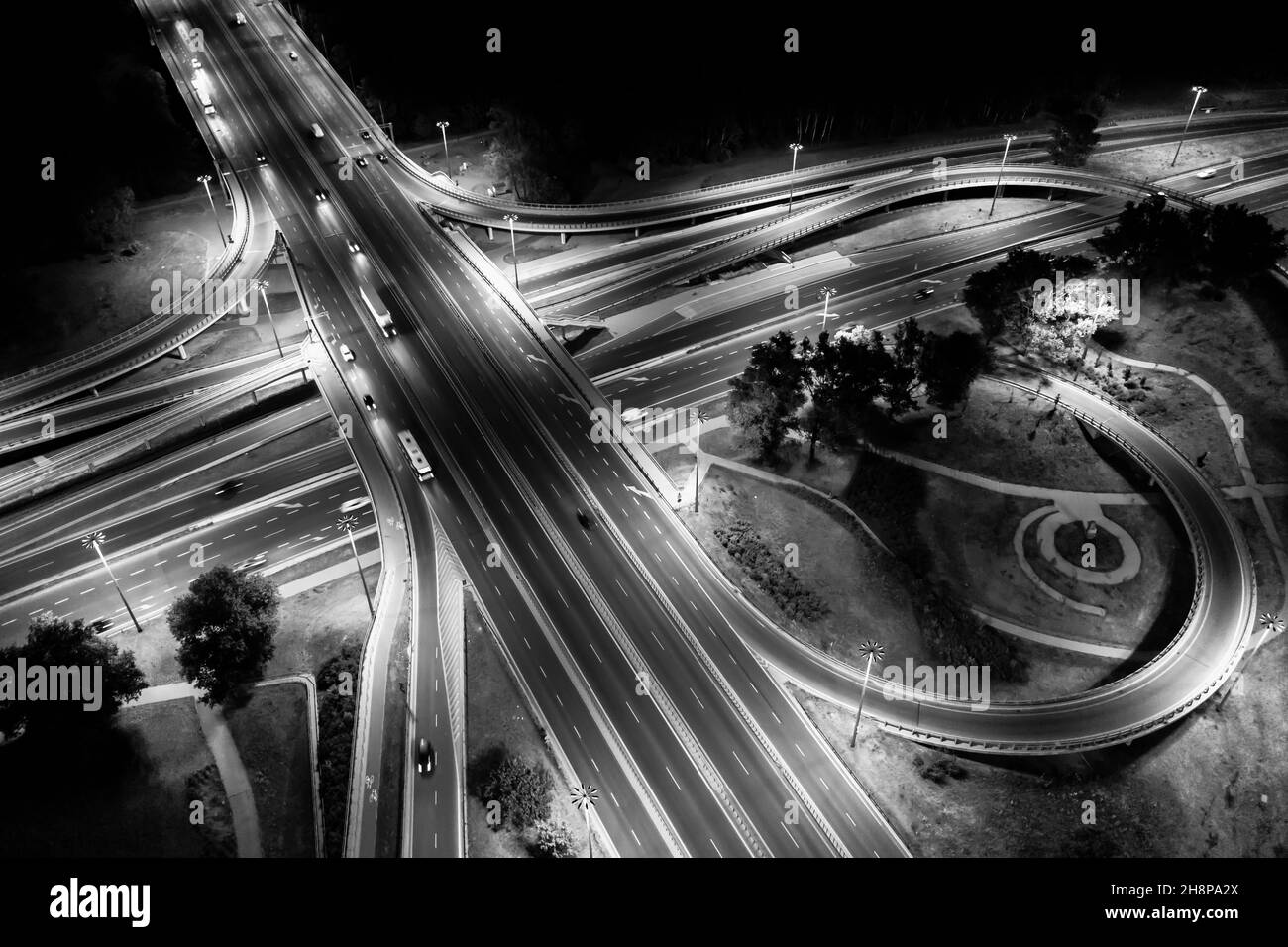 Aerial drone night shot of multilevel illuminated ring highway road junction leading to the sea. Black and White Stock Photo