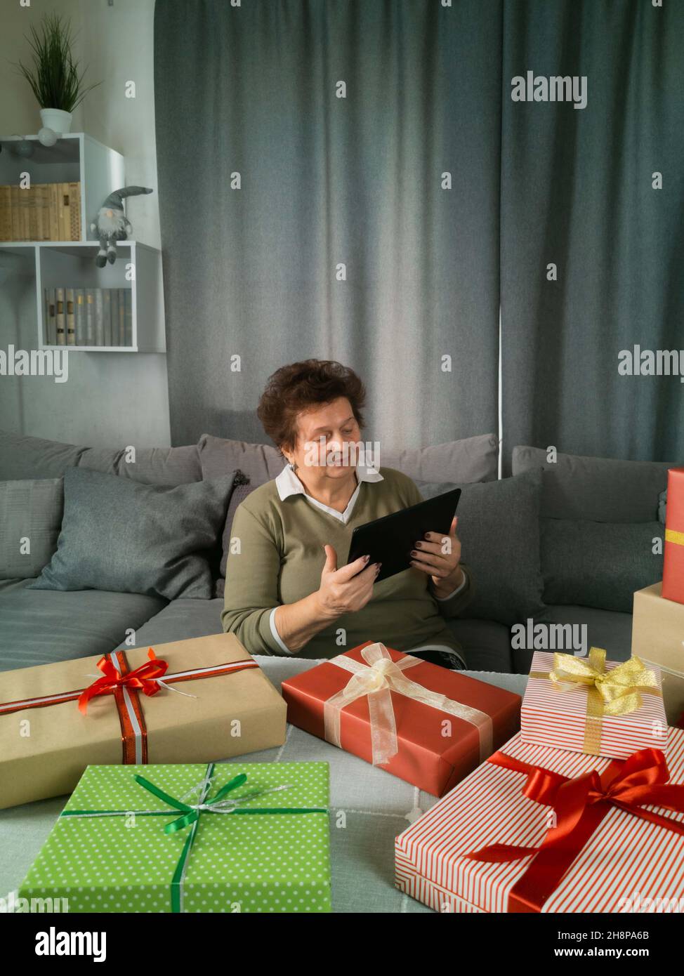 https://c8.alamy.com/comp/2H8PA6B/an-elderly-woman-is-packing-gifts-and-holding-a-tablet-in-her-hands-2H8PA6B.jpg